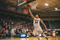 High school basketball player mid-air on fastbreak dunk in packed tournament gym with OGP banners in background